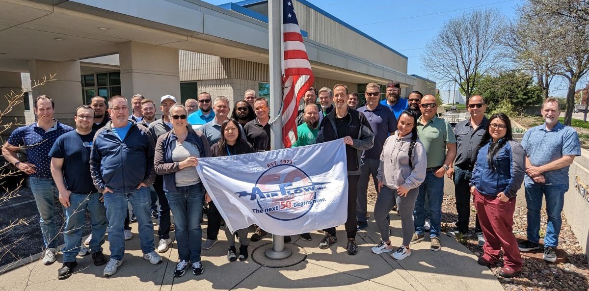 Air Flow team standing outside of office building with anniversary flag
