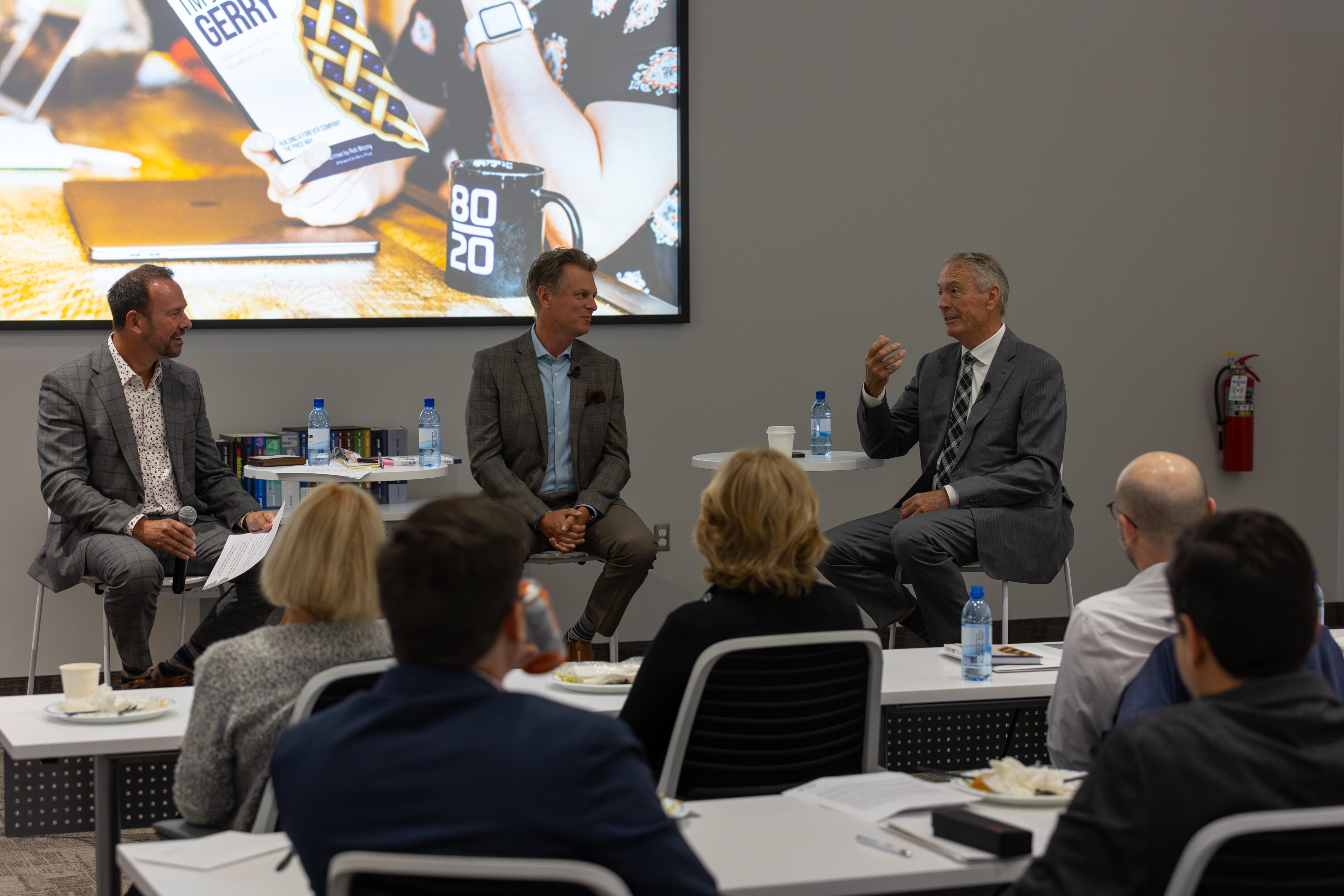 Greg Loeppky, Rob Wozny and Gerry Price sitting in front of a crowd of employees