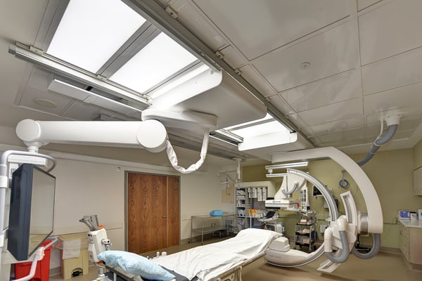 Operating room with ceiling mounted medical equipment surrounding table and laminar diffusers with integrated lighting