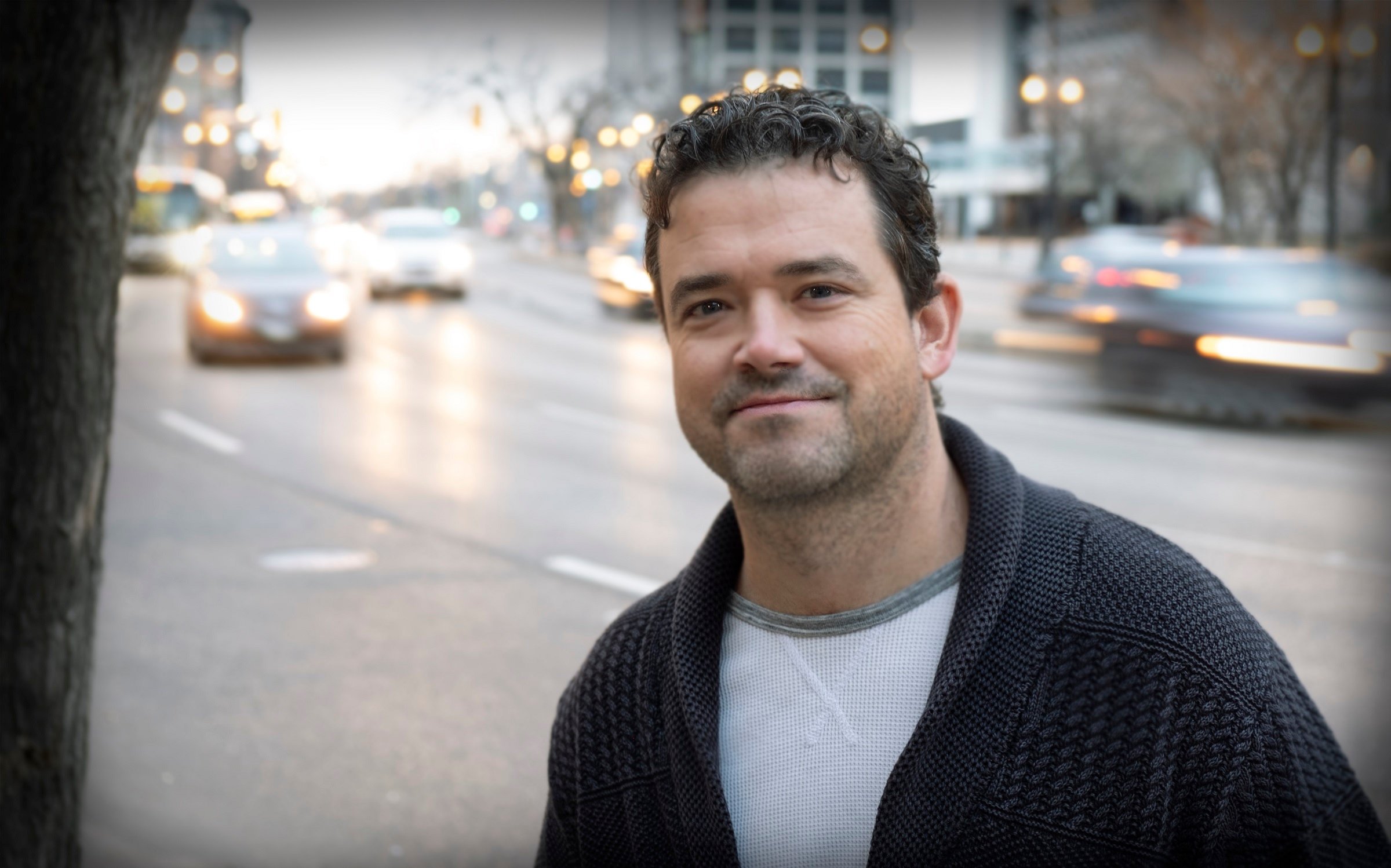 Justen Vogt smiling while standing outdoors near a busy street filled with traffic.