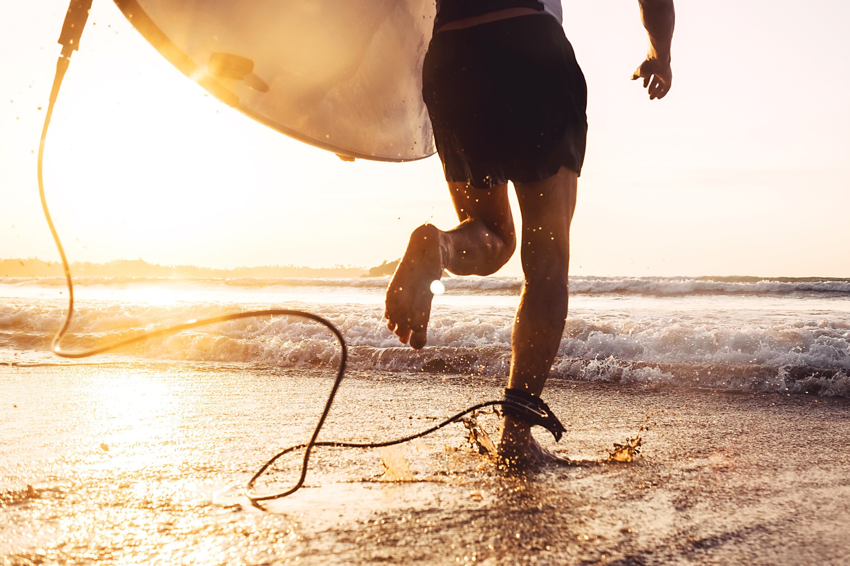 Person running with surfboard on beach